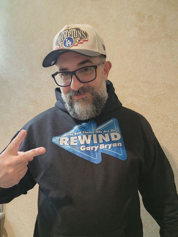 Man wearing a white baseball cap, eyeglasses and a black hoodie with the Rewind with Gary Bryan logo on the front.